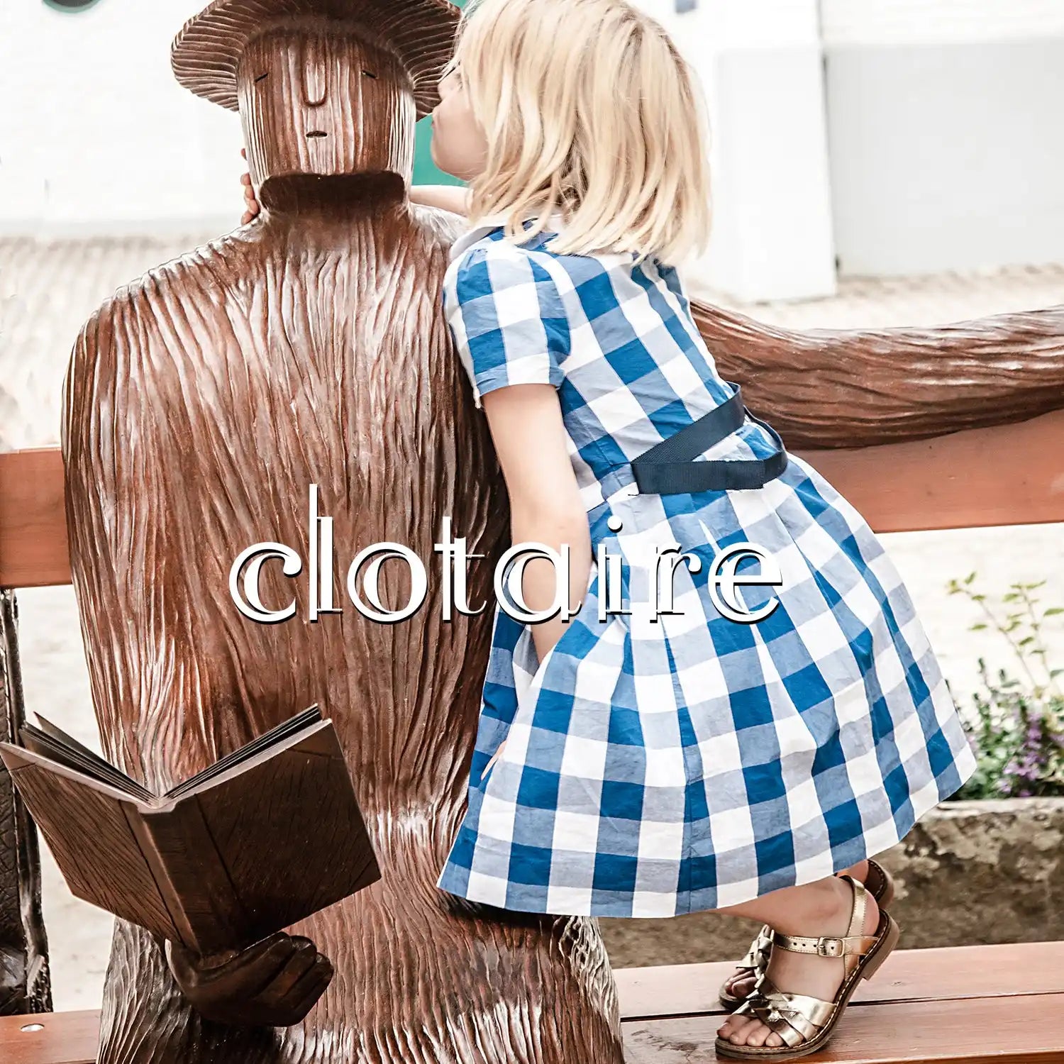 Sculpture en bois d'une figure assise sur un banc en train de lire un livre.