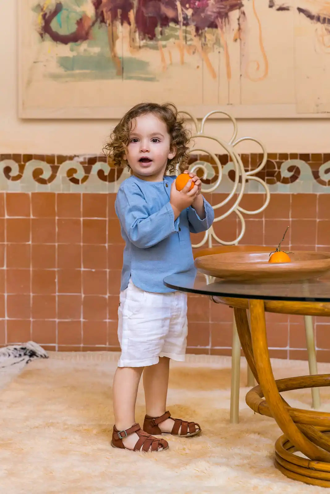 Un tout-petit dans un pull bleu et un short blanc tenant un jouet orange.
