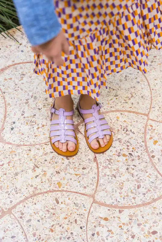 Lilac leather gladiator sandals with multiple straps worn with a plaid dress.