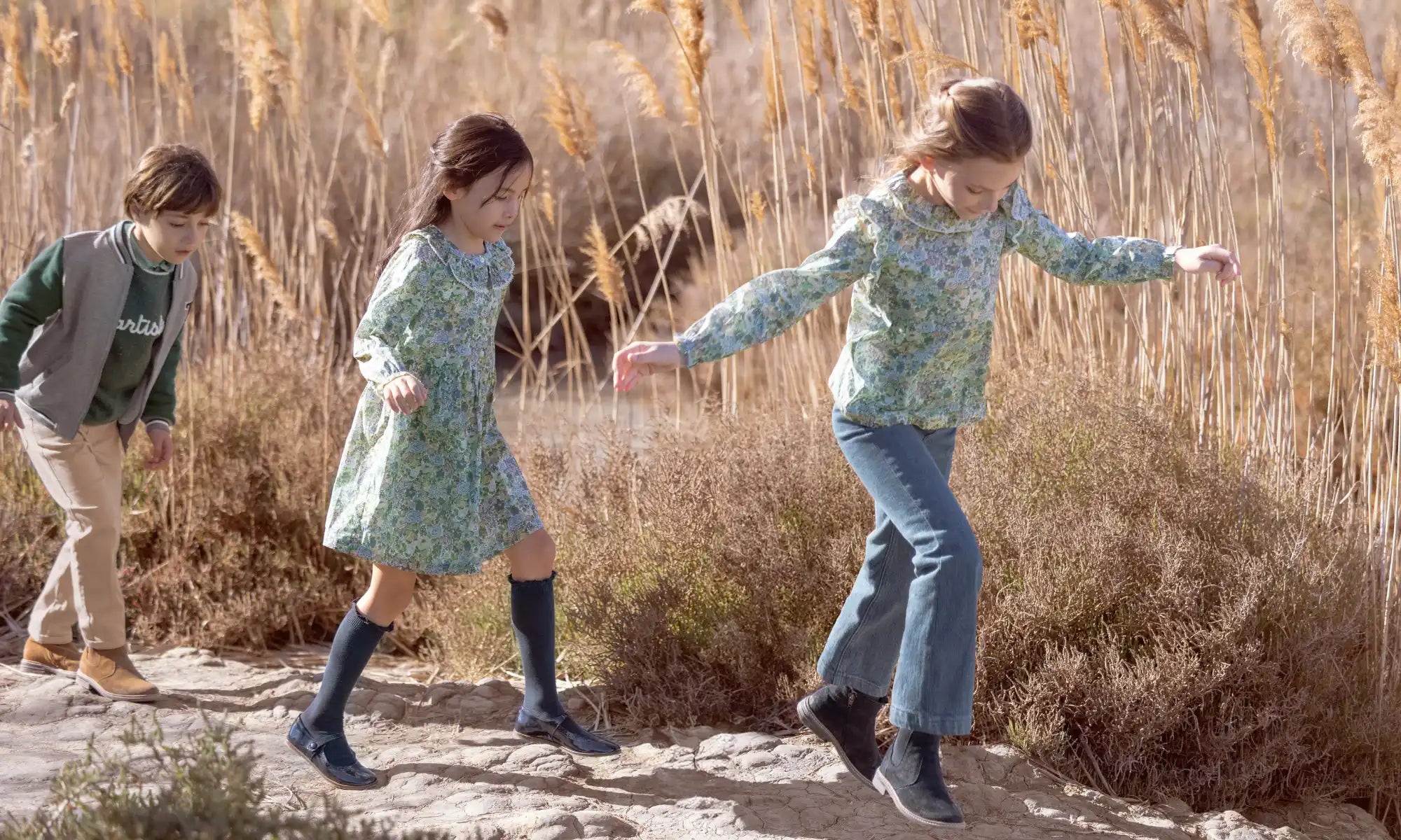 Three people walking in a line along a path wearing casual autumn clothing.